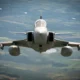 Front view of a fighter jet flying toward the camera over a green valley