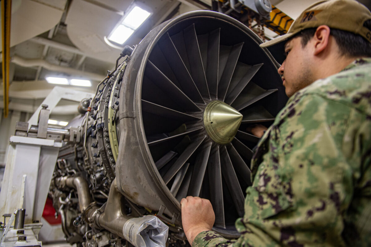 USS Ronald Reagan CVN 76 Sailors perform daily maintenance Military technician in camouflage uniform inspecting the interior of a large jet engine turbine in a hangar