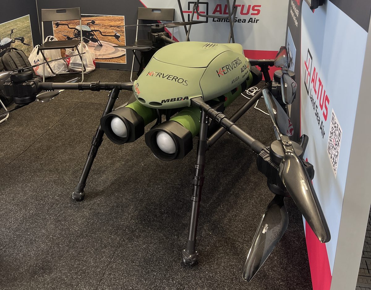 ALTUS LSA Kerveros drone displayed with two Akeron MP missile models Large quadcopter drone on display in a showroom green body with logos four rotor arms and landing legs visible