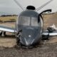 Small grey airplane crashed on a gravel surface nose damaged and cockpit canopy intact wings wide and landing gear damaged nearby