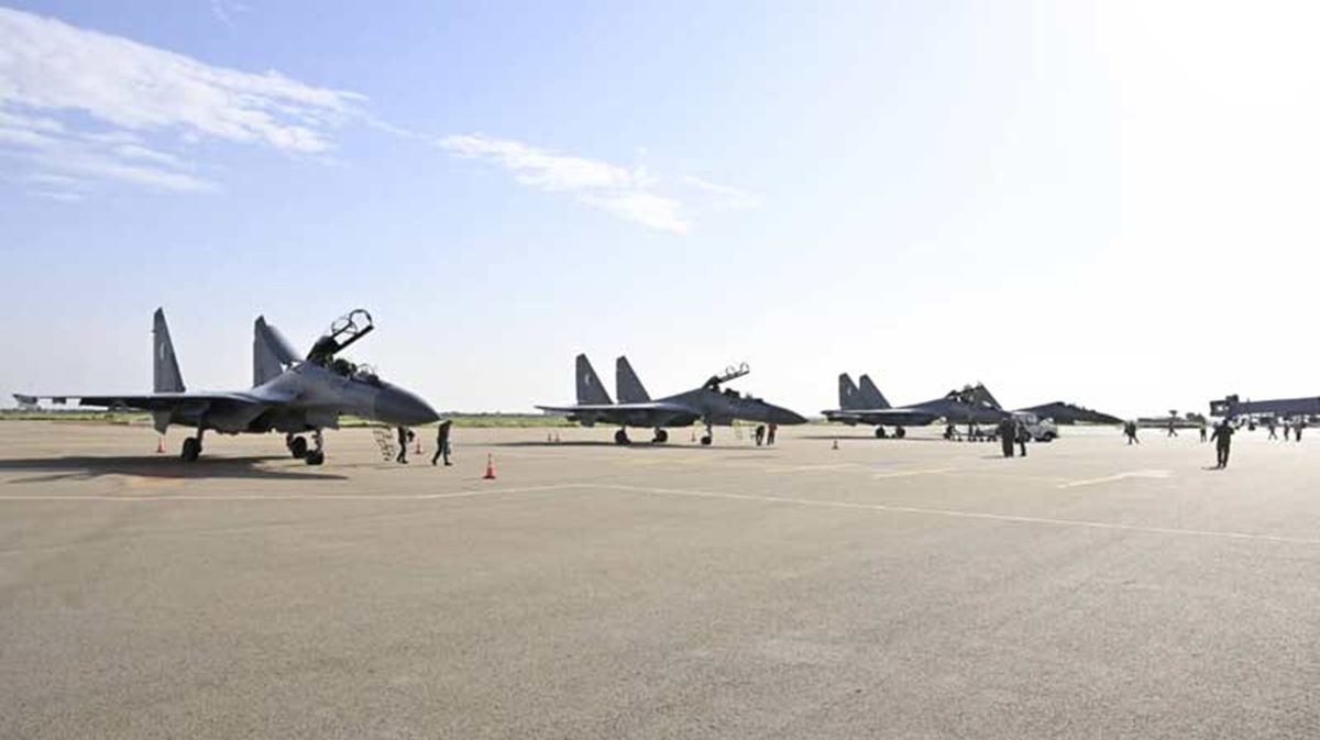 Algerian Air Force Su 30 fighters at Niamey airport Row of gray military fighter jets parked on a sunlit airfield with ground crew walking nearby in a spacious tarmac area