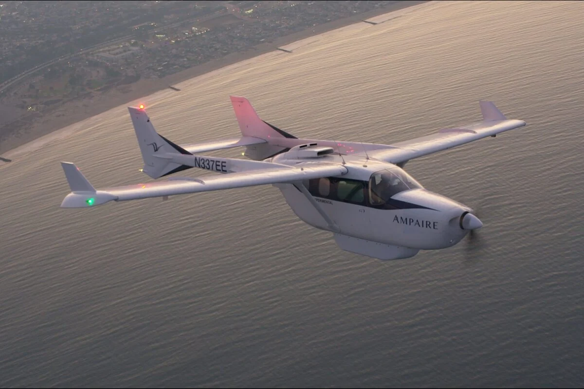 White Ampaire light aircraft with registration N337EE flying over the ocean near the coastline sunset light reflecting on water