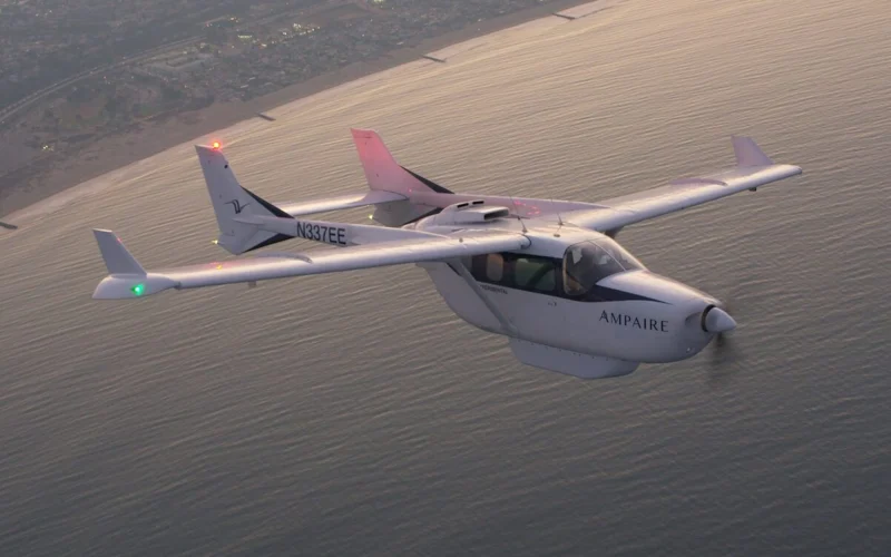 White Ampaire light aircraft with registration N337EE flying over the ocean near the coastline sunset light reflecting on water