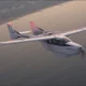 White Ampaire light aircraft with registration N337EE flying over the ocean near the coastline sunset light reflecting on water