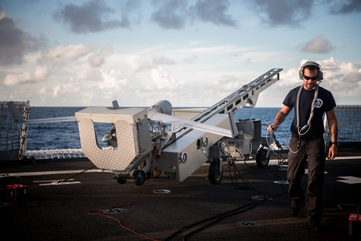 Coast Guard Cutter Stratton participates in Talisman Sabre 2019 Crew member in a dark Tshirt and headset stands beside a large gray launch apparatus on a ship deck ocean in the background