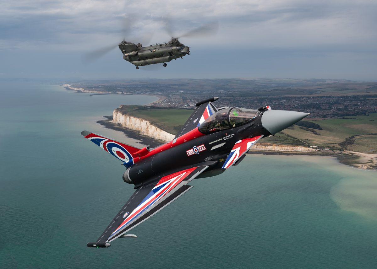An RAF Typhoon FGR4 and Chinook helicopter fly together near Beachy Head during a training sortie in 2022 Aerobatic jet with Union Jack livery flies low over coastline with a Chinook helicopter passing nearby above the sea and cliffs