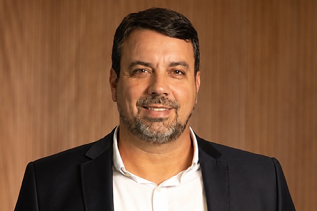 Head and shoulders portrait of a smiling man in a dark blazer and white shirt against a wood background