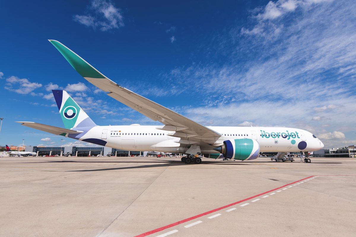 Airliner on the tarmac with large angled wingtip white fuselage with teal accents and a colorful tail at an airport