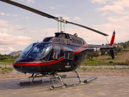 Black helicopter on a concrete pad with a red stripe and the word Bellavia visible on the fuselage rural landscape in the background