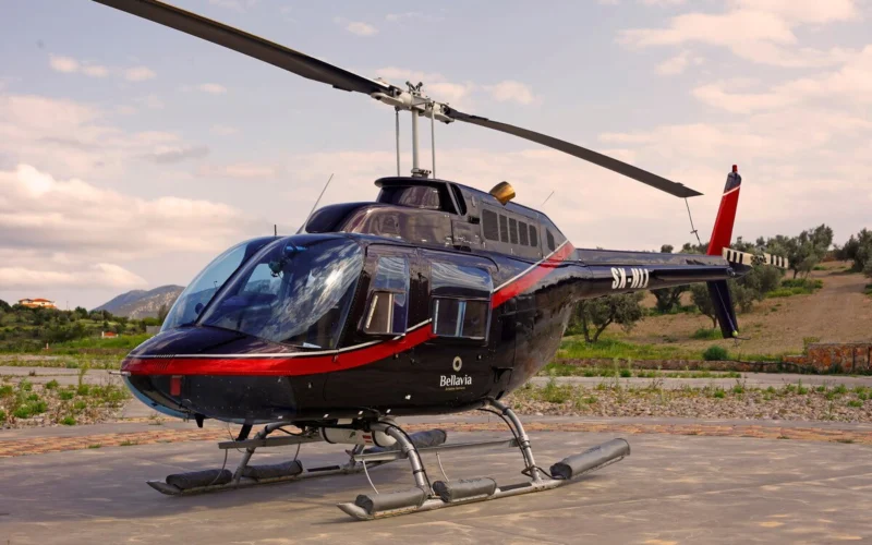 Black helicopter on a concrete pad with a red stripe and the word Bellavia visible on the fuselage rural landscape in the background