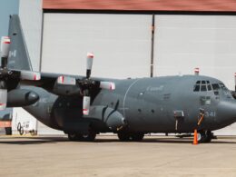 Canada marked military C 130 Hercules turboprop aircraft on a tarmac in front of a hangar propellers visible on both wings