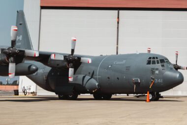 Canada marked military C 130 Hercules turboprop aircraft on a tarmac in front of a hangar propellers visible on both wings