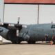 Canada marked military C 130 Hercules turboprop aircraft on a tarmac in front of a hangar propellers visible on both wings