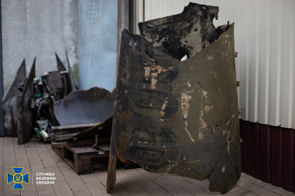 Fragments of North Korean Hwasong 11 KN 23 ballistic missiles recovered after Russian strikes on Ukraine Charred dented metal barrel outdoors with rubble and pallets nearby Ukrainian Security Service SBU logo visible in the bottom left corner