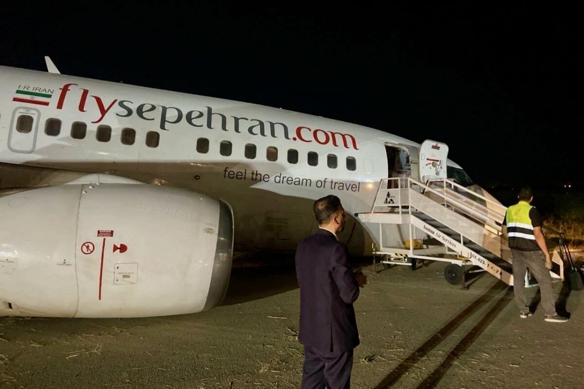 Nighttime at the airport a FlySepehran airplane with boarding stairs attached and ground crew nearby reflective vests visible in the scene dark sky behind