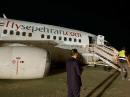 Nighttime at the airport a FlySepehran airplane with boarding stairs attached and ground crew nearby reflective vests visible in the scene dark sky behind