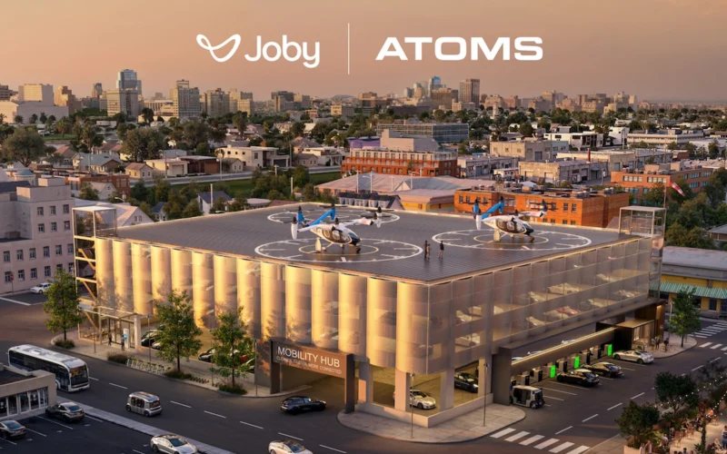 Aerial view of a modern Mobility Hub building with two rooftop helicopters and a city skyline showing Joby and ATOMS branding
