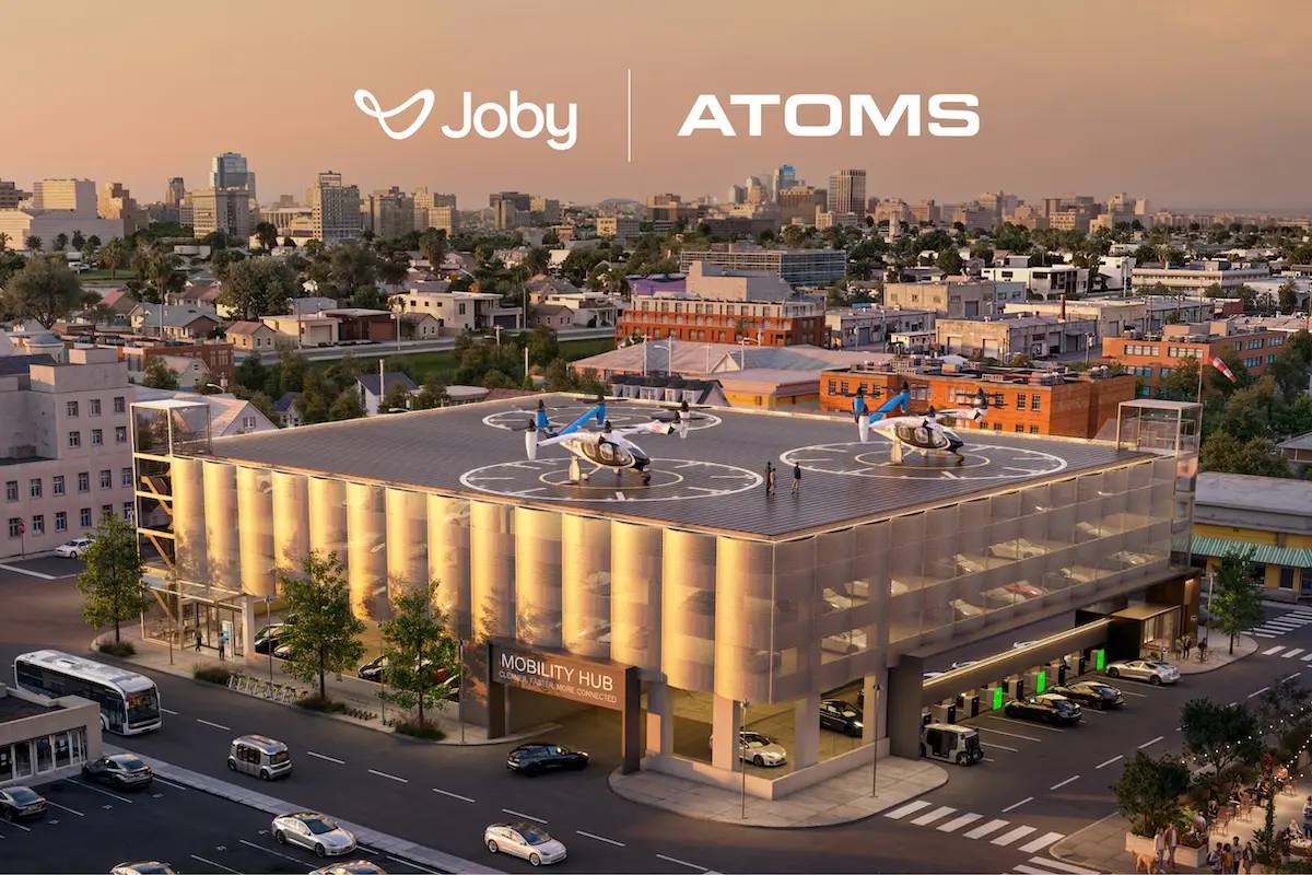 Joby Atoms Vertiport Render Aerial view of a modern Mobility Hub building with two rooftop helicopters and a city skyline showing Joby and ATOMS branding