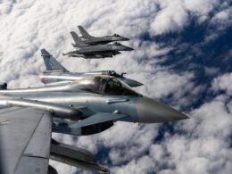 Three silver fighter jets in tight formation flying above a cloudy blue sky