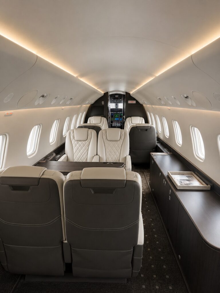 PJ L650 interior Prime GroupSeating 1 Luxurious private jet cabin with beige leather seats dark wood sideboard and ambient lighting along the ceiling