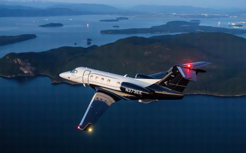 Private jet in flight over a blue sea with forested islands and distant mountains at dusk tail number N373EE visible on the fuselage