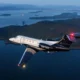 Private jet in flight over a blue sea with forested islands and distant mountains at dusk tail number N373EE visible on the fuselage
