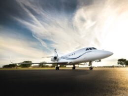 Front right view of a white corporate jet parked on a runway blue sky and dramatic clouds above
