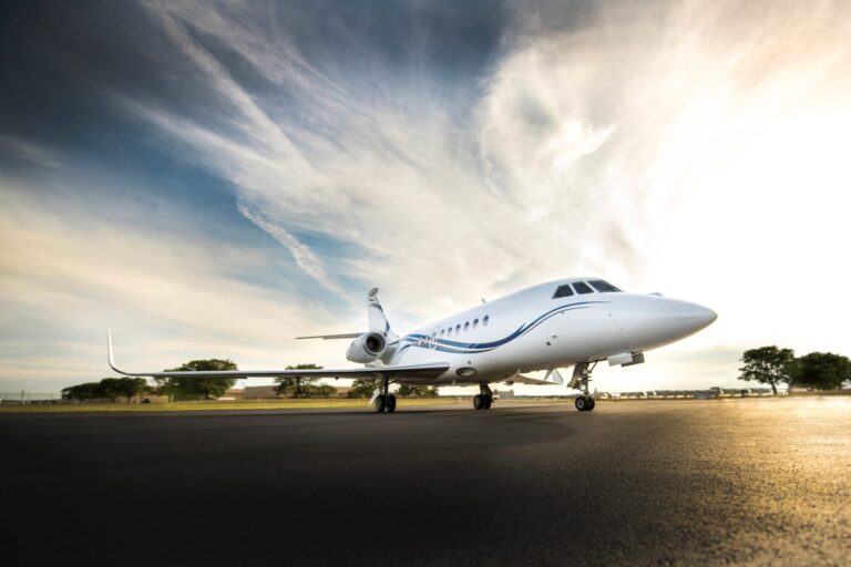 Front right view of a white corporate jet parked on a runway blue sky and dramatic clouds above