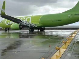 Bright green passenger plane on a wet tarmac viewed from the side with engines under the wings