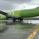 Bright green passenger plane on a wet tarmac viewed from the side with engines under the wings