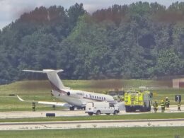 White private jet on the runway with firefighters and a yellow fire truck nearby