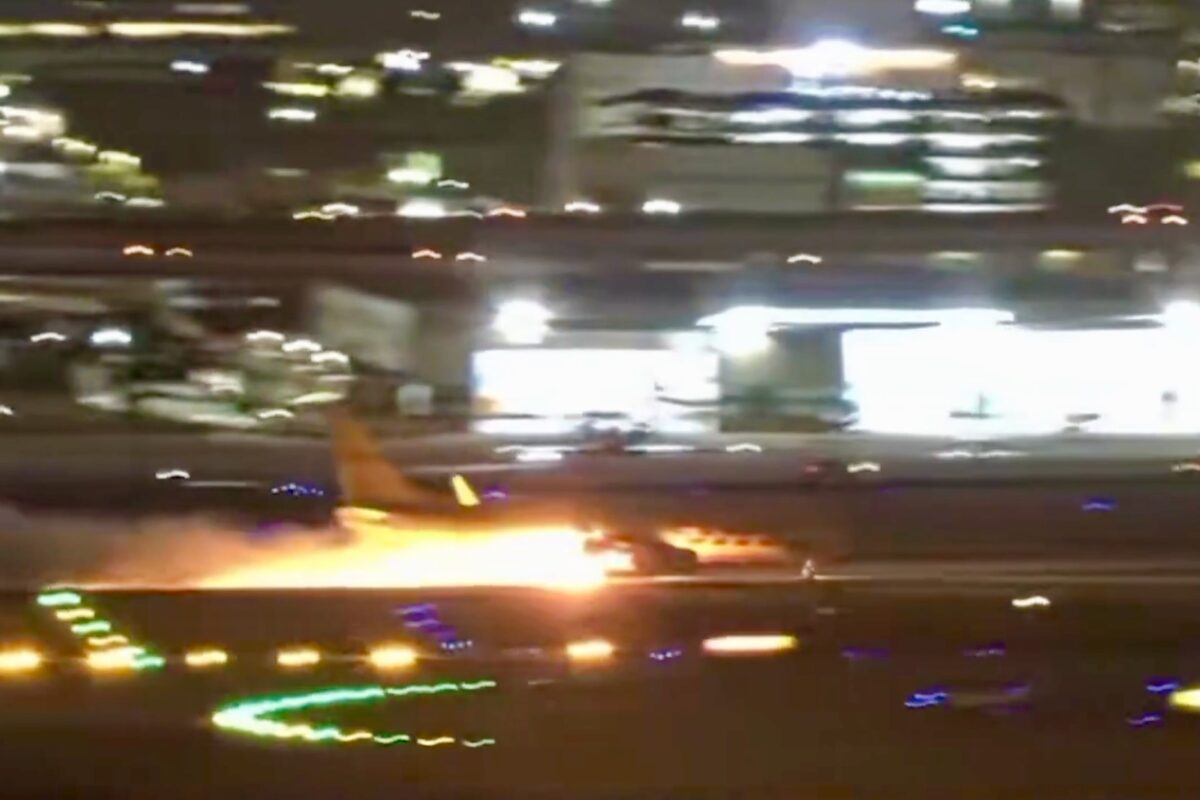 Screenshot Nighttime airport scene a blurred aircraft on the runway with bright flames or exhaust nearby and city lights in the background on a hazy night