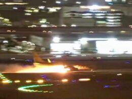 Nighttime airport scene a blurred aircraft on the runway with bright flames or exhaust nearby and city lights in the background on a hazy night