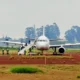 White passenger jet on a tarmac with mobile stairs attached to the forward door and ground crew nearby preparing for boarding