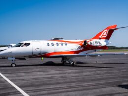 White private jet with red and orange accents parked on a runway under a clear blue sky registration N378PG visible on the tail
