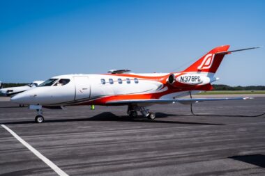 White private jet with red and orange accents parked on a runway under a clear blue sky registration N378PG visible on the tail