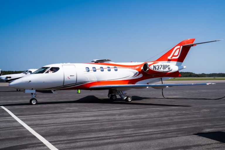 White private jet with red and orange accents parked on a runway under a clear blue sky registration N378PG visible on the tail