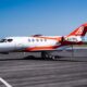 White private jet with red and orange accents parked on a runway under a clear blue sky registration N378PG visible on the tail
