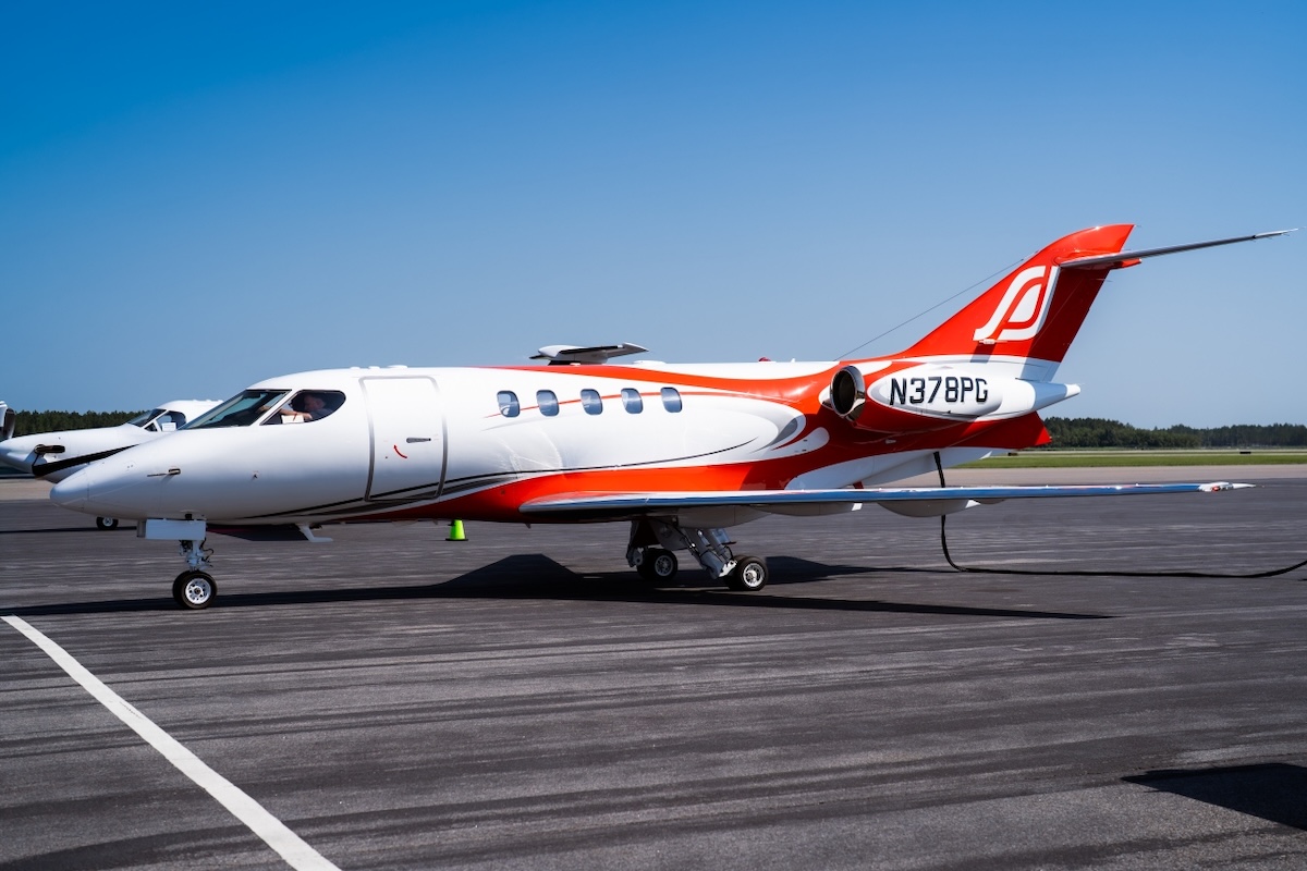 White private jet with red and orange accents parked on a runway under a clear blue sky registration N378PG visible on the tail