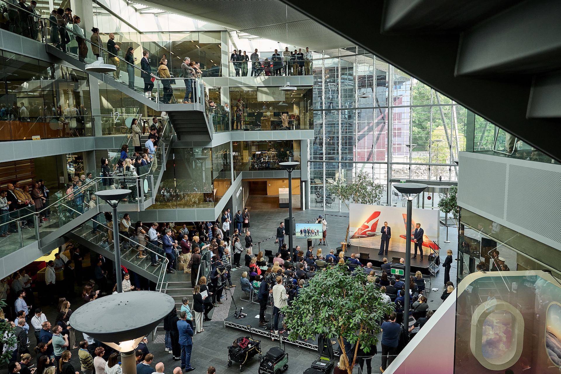 The Street during the FY26 results presentation in Mascot Busy modern atrium filled with people at a conference a speaker on stage addresses a seated and standing audience across multiple glass walled levels