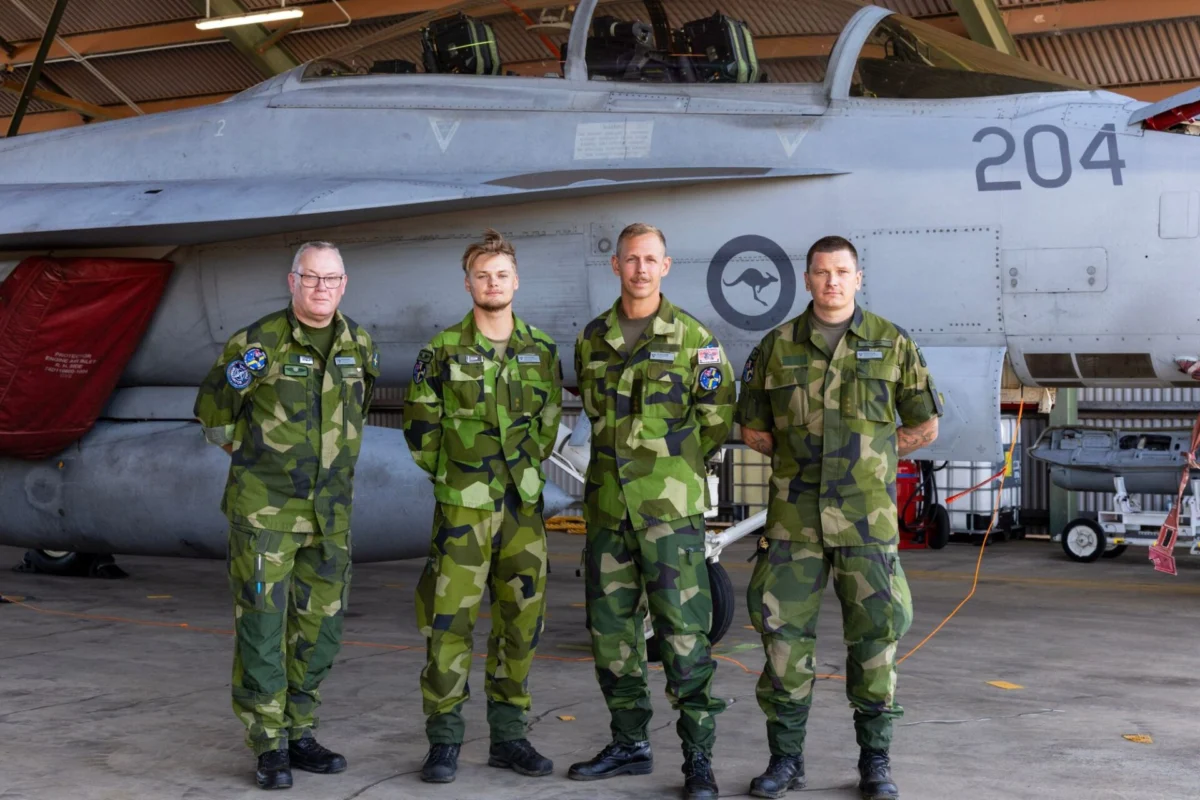 Finland and Sweden make first appearance to RAAF Pitch Black Four air force personnel in camouflage uniforms stand in front of a fighter jet inside a hangar