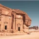 Ancient sandstone temple carved into a red cliff featuring arched doorways and decorative pediments in a desert landscape