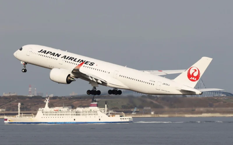 Japan Airlines jet taking off over the water side view with the red JAL crane logo on the tail