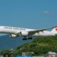 Japan Airlines passenger jet with landing gear down flying low above green hills against a blue sky