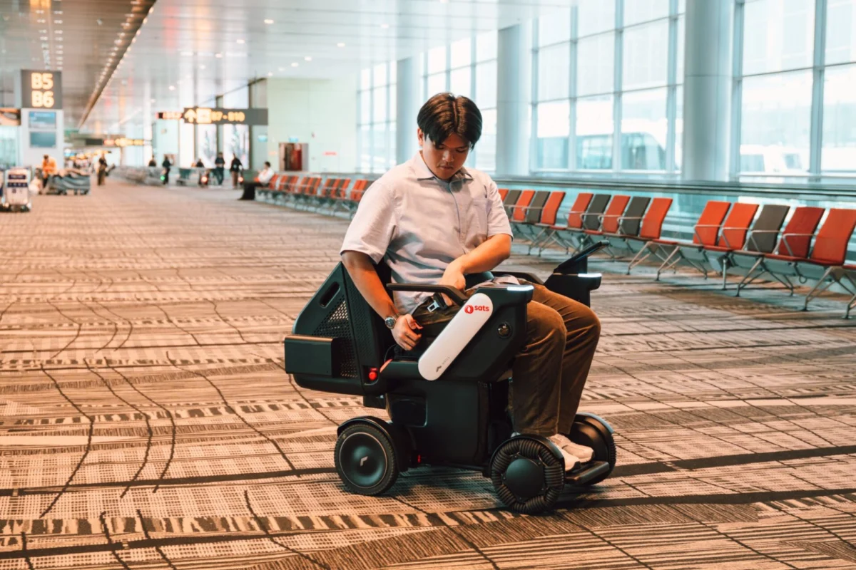 Changi rolls out autonomous wheelchairs for travelers Man in a light shirt sits on a mobility scooter in an airport terminal looking at the control paneltablet in his hands