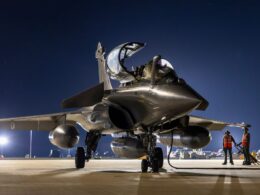 Fighter jet on a night time runway with cockpit open and two ground crew in orange vests nearby