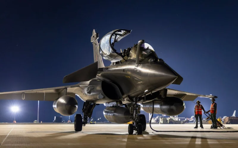 Fighter jet on a night time runway with cockpit open and two ground crew in orange vests nearby