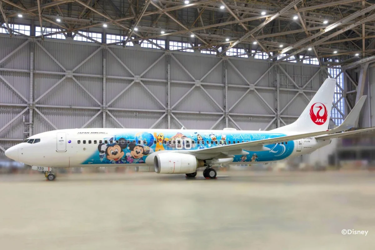 JAL unveils Tokyo DisneySea anniversary themed aircraft Japan Airlines plane in a hangar with a Disney themed livery featuring Mickey Mouse characters JAL red tail logo visible