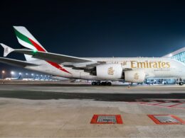 Emirates wide body jet parked at night on an airport tarmac with terminal building in the background