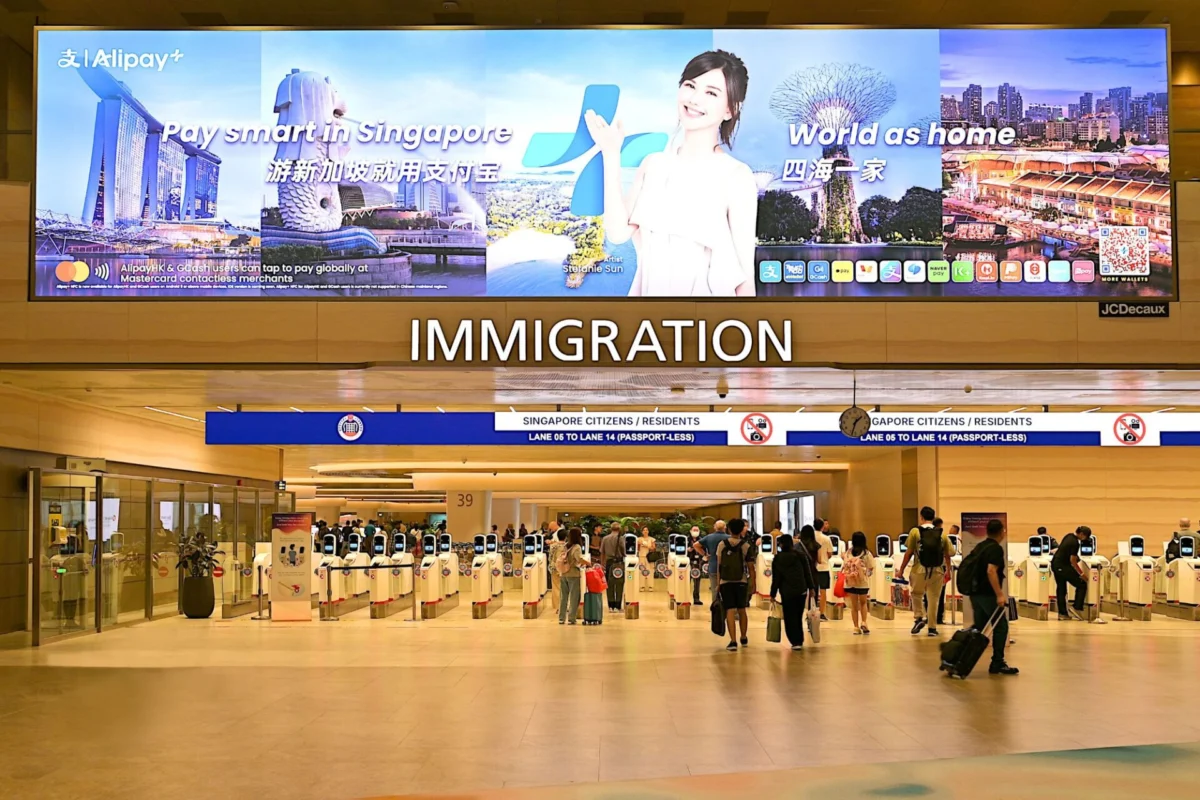 Large immigration hall at an airport with a row of self service kiosks and a prominent IMMIGRATION sign above travellers queuing